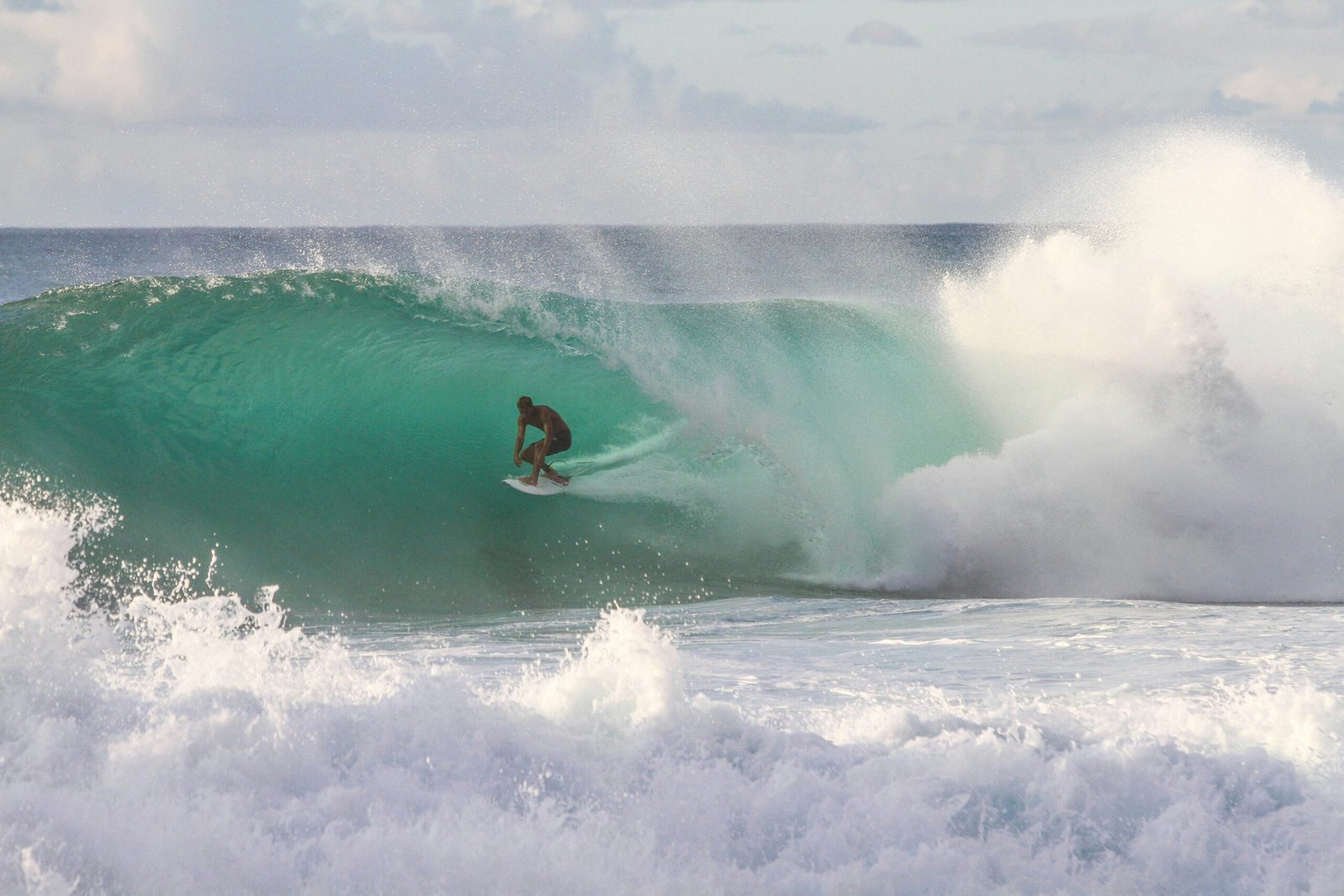 A photo of a surfer riding a large wave on the North Shore of Oahu, Hawaii. The surfer is standing on the surfboard, with the wave cresting above them. The sky is blue and clear. [Photo by Jeremy Bishop on Unsplash]